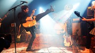 Gitarrist von Angelika Express streckt sein Bein in die Luft und spielt ein heißes Solo auf seiner Gibson Halbakustik E-Gitarre