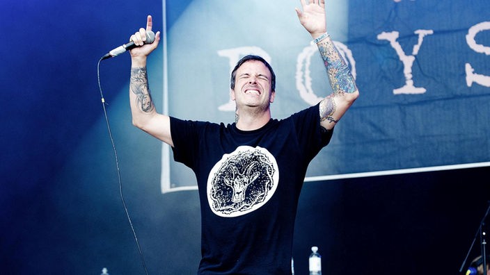 Der Sänger reißt die Hände nach oben, seine Tattoos sind gut zu erkennen