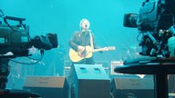 Wolfgang Niedecken steht auf der blau erleuchteten Bühne und wird von Kameras gefilmt