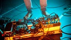 Nackte Füße eines Musikers vor einem Effektboard im blauen Scheinwerferlicht