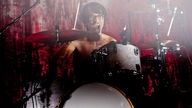 Schlagzeuger von Bloc Party vor rotem Hintergrund mit nacktem Oberkörper und offenem Mund