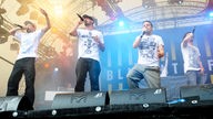 4 Jungs mit Mikrofon im weissen T-shirt nebeneinander auf der Bühne