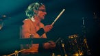 Drummer von "The Chuck Norris Experiment" spielt mit nacktem Oberkörper Schlagzeug.
