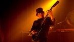 Gitarrist von "Hong Faux" mit Hut im gelben Scheinwerferlicht.