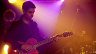 Chakuza-Gitarrist spielt im pink-gelben Scheinwerferlicht
