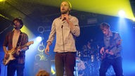 Gitarrist, Sänger und Bassist von OK KID auf der Bühne im gelb-blauen Licht.