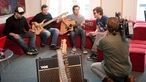 Die Band Jonas & The Massive Attraction sitzen auf einer Couch und spielen ihre Instrumente. Ein Kameramann filmt das Geschehen.