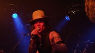 Der Sänger von Doomfoxx bei Bootleg im April 2006 in recht dunklem roten Licht mit einem großen Hut.