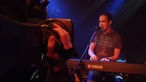 Im Vordergrund ist eine große Kamera bei Bootleg im April 2006 zu sehen, hinter welcher der Frontmann von Rivo Drei an seinem Keyboard steht und singt.