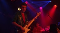 Der Bassist der Band Rivo Drei steht bei Bootleg im April 2006 auf der Bühne in dem rosanen Licht der Scheinwerfer.