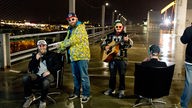 Mc Fitti und Band auf Parkoberdeck bei Nacht mit beleuchteter City im Hintergrund 