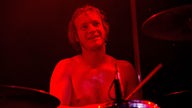 Ein Portrait des in rotes Licht getauchten Schlagzeugers der Band Birth of Joy.