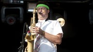 Saxophonist mit armbändchen und grünem schweißhaarband und gelben streifen im gesicht