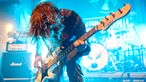Bassist spielt mit angewinkelten Beinen, nach vorne gebeugt im blauen Licht
