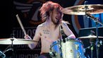 Drummer Pete Flett wirbelt die Drumsticks, seine langen Haare fliegen umher. Er spielt bei nacktem Oberkörper und hat mehrere Tatoos.