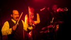 Drummer und Bläser von "The Inspector Cluzo & The FB's Horns" im roten Bühnenlicht