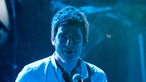 Noel Gallagher ist in blaues Licht getaucht und sieht genau in die Kamera.
