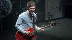 Noel Gallagher singt mit voller Kraft in sein Mikrofon.