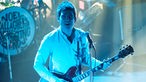 Noel Gallagher ist in blaues Licht getaucht und sieht direkt in die Kamera.