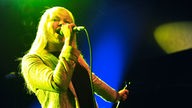 Die blonde Sängerin von The Duke Spirit singt ins Mikrofon und ist in gelbes Scheinwerferlicht gehüllt 
