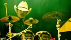 Ein Mann mit Cowboyhut und Schnauzbart sitzt vor einem Schlagzeug