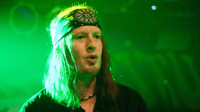 Mann mit langen Haaren und Kopftuch im grünen Bühnenlicht