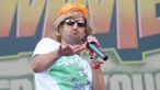 Ein Sänger der Ohrbooten trägt eine blonde Perücke mit orangem Hut und Sonnenbrille und verzieht den Mund.