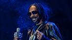 Snoopdog hält ein Mikrofon in der Hand und lacht