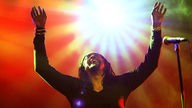 The I.M.F´s Sänger mit ausgebreiteten Armen nach oben, dahinter helles Licht