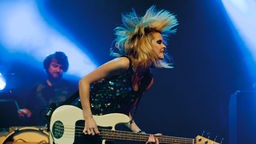 Die Sängerin der Band buegt sich mit Ihrer Gitarre nach vorne und wirft dabei ihre Haare durch die Luft