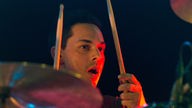 Drummer hält zwei Drumsticks hoch, den Mund konzentriert geöffnet und von der Anstrengung verschwitzt.