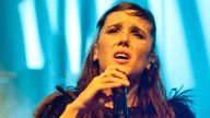 Zaz singt mit leidendem Gesichtsausdruck vor blauem Hintergrund
