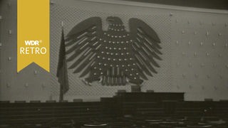 Großaufnahme des Reichsadlers, der in einem Saal mit vielen Sitzmöglichkeiten an der Wand abgebildet ist.