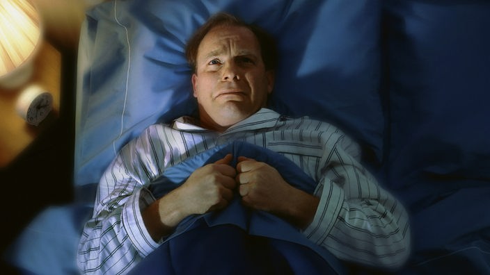 Mann verzweifelt nachts im Bett sitzend
