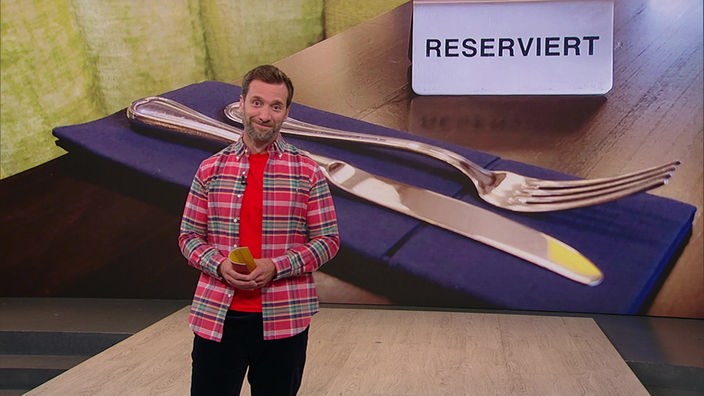 Daniel Aßmann steht in einem Fernsehstudio. Hinter ihm ist ein Tisch mit einem "Reserviert"-Schild zu sehen.