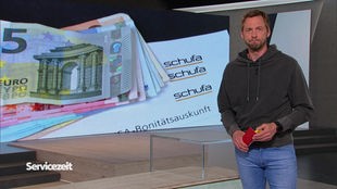 Der Moderator im SZ-Studio vor einem Bild von Geldscheinen, die auf einem Brief der Schufa liegen