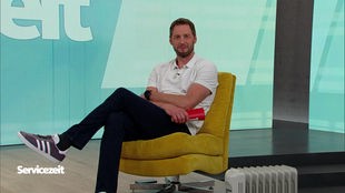 Der Moderator sitzt auf einem gelben Stuhl im Servicezeit-Studio