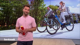 Der Moderator im SZ-Studio vor einem Bild vor zwei E-Bike-Fahrern