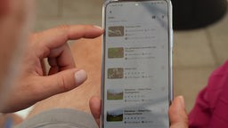 Das Bild zeigt ein Handy, auf dem eine App bedient wird. 