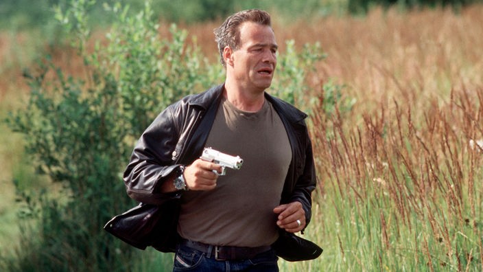 Max Ballauf (Klaus J. Behrendt) auf Verbrecherjagd. Mit gezogener Pistole verfolgt er den Serienmörder.