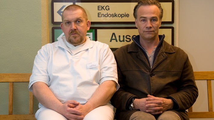 Max Ballhauf (Klaus Johannes Behrendt) und Freddy Schenk (Dietmar Bär) sitzen auf einer Bank im Krankenhaus.