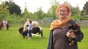 Eine rothaarige Frau hält einen kleinen Hund im Arm, im Hintergrund sind Menschen mit Ponys