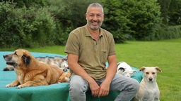 Andreas Ohligschläger sitzt mit Hunden auf einer Wiese und schaut in die Kamera