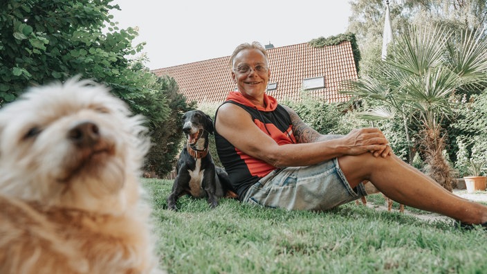 Tierschützer Dirk Vinkemöller sitzt mit zwei Hunden auf einer Wiese 