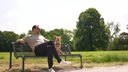 Ein Mann und ein Hund mit hellem Fell sitzen auf einer Parkbank in der Sonne 