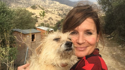 Moderatorin Simone Sombecki steht in griechischen Bergen und hält einen Hund im Arm
