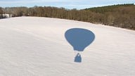 Schatten eines Heißluftballons auf Schneelandschaft.