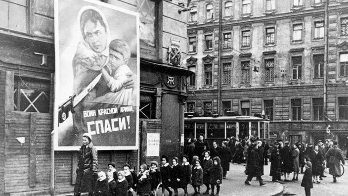 Eine Kindergruppe läuft vor einem Plakat entlang, das zur Verteidigung der sowjetischen Heimat aufruft, aufgenommen 1942