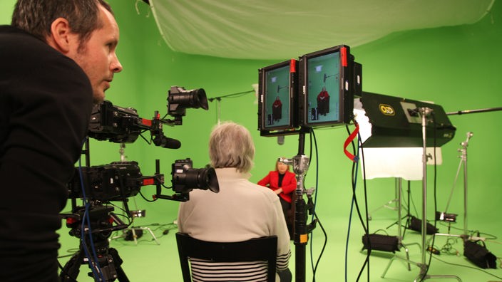 Eine Frau wird in einem Green Screen-Studio interviewt, ein Filmemacher kontrolliert die Kamera-Einstellungen.