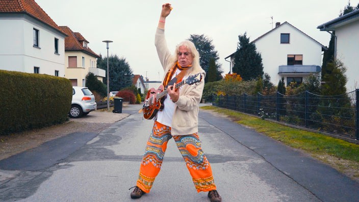 Der Missus-Beastley-Gitarrist und Alt-Hippie ArtZen posiert in einer Wohnstraße mit einer E-Gitarre.